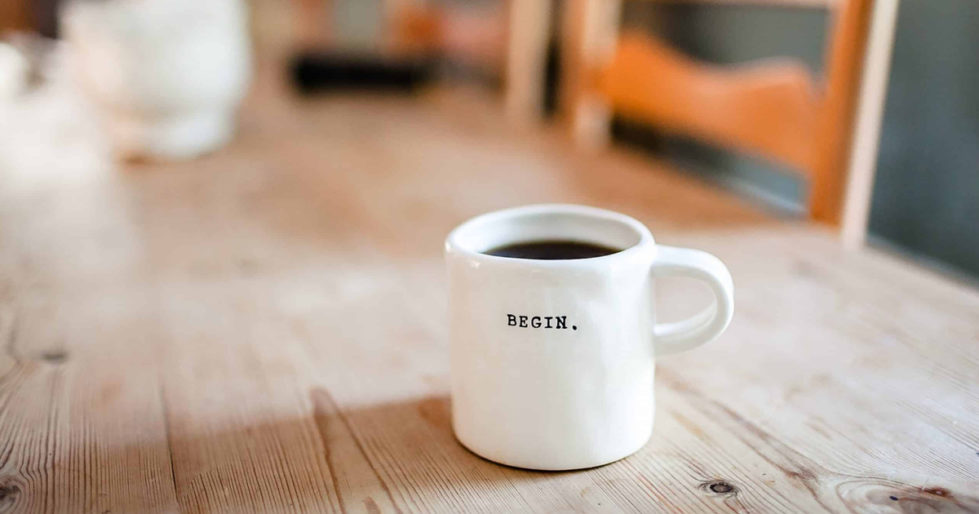 a coffee cup on a wooden table with the word "Begin" printed on it.