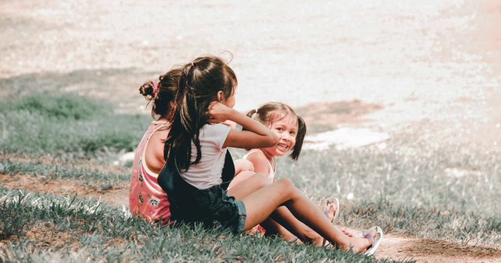 3 children sit together on the grass