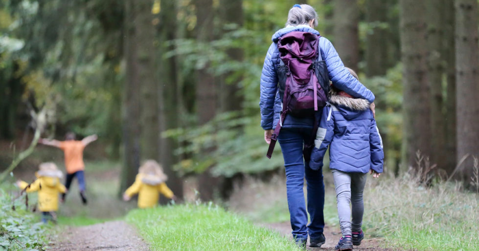 A mother with her arm around a child walk into the forest, while the rest of the family runs ahead.