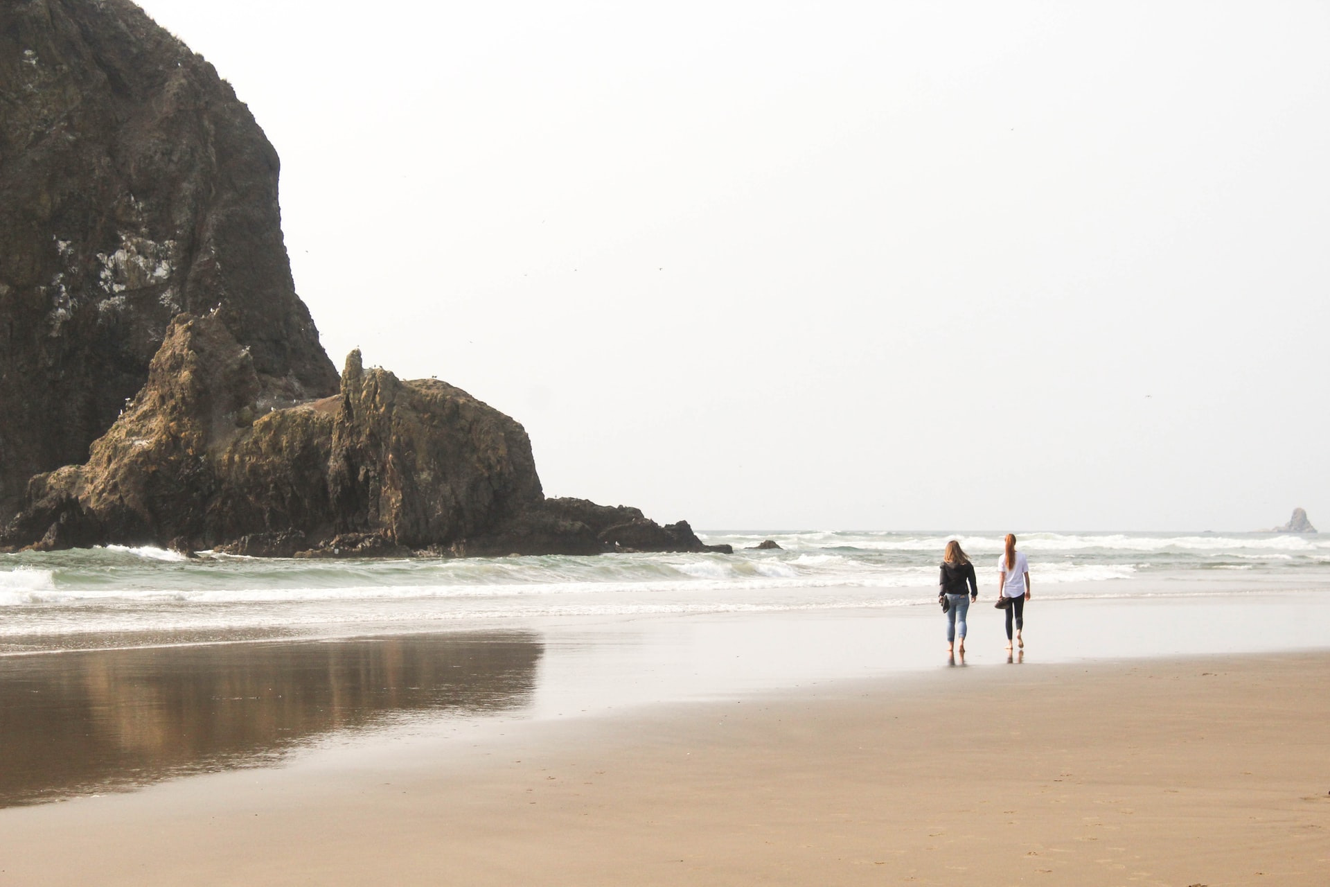 Two women walk barefoot on a large, sandy beach