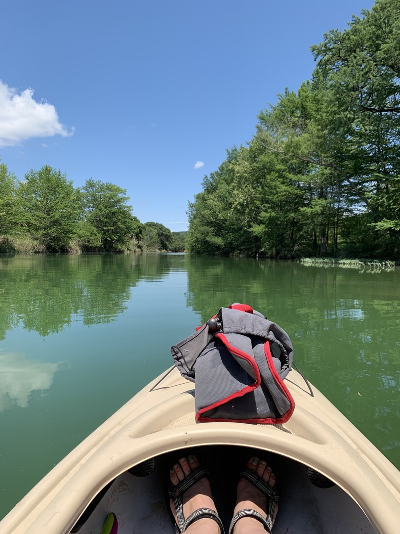 A picture of a pair of feet in a canoe on calm, green water