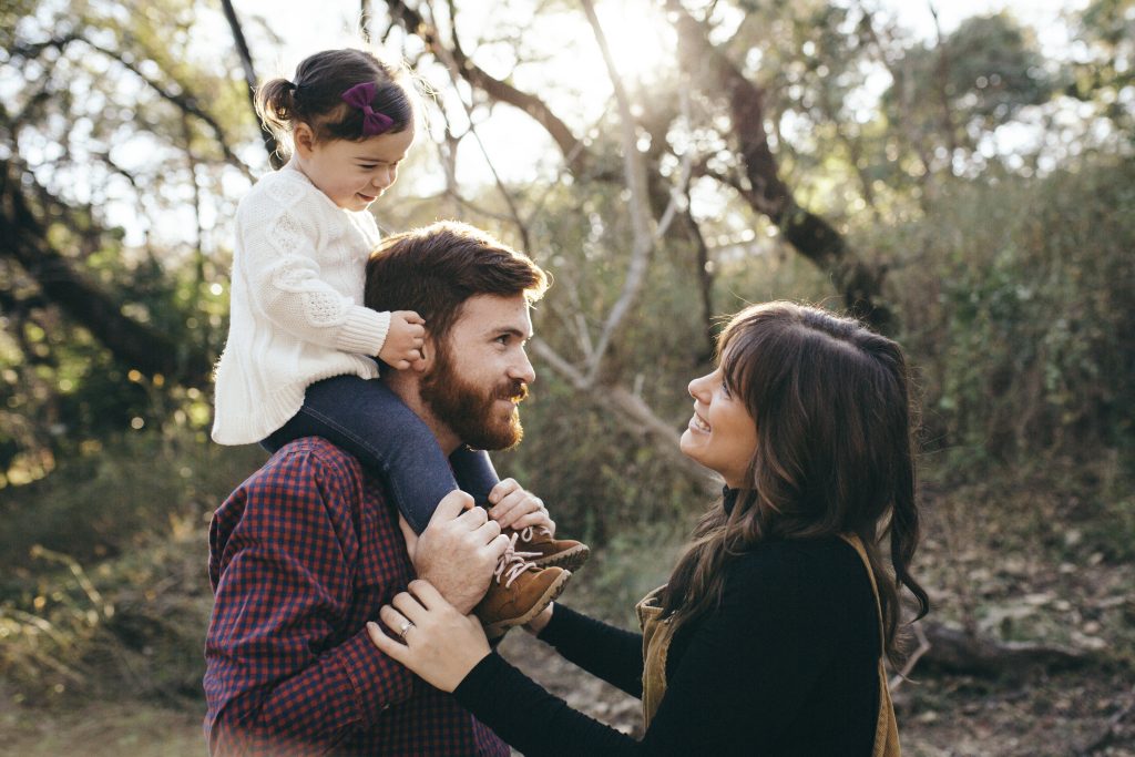 Chelsea gazes at her child who's sat atop her husbands shoulders