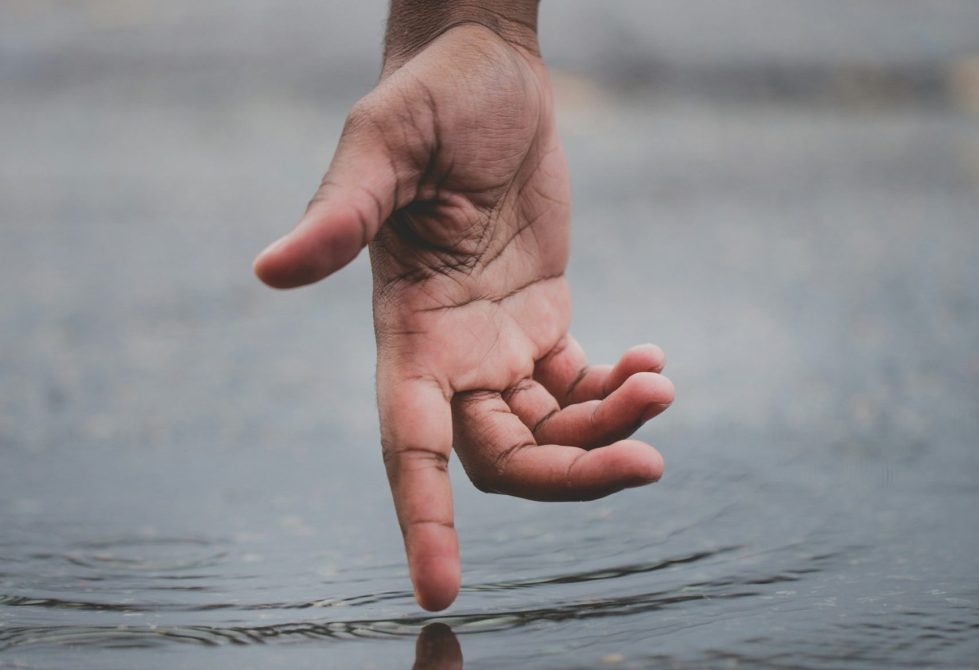 Black hand touching a ripple in body of water